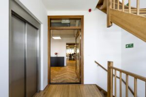 Ingang van een modern kantoor aan de De Ruijterkade met zicht op houten trap, lift en vergaderruimte.